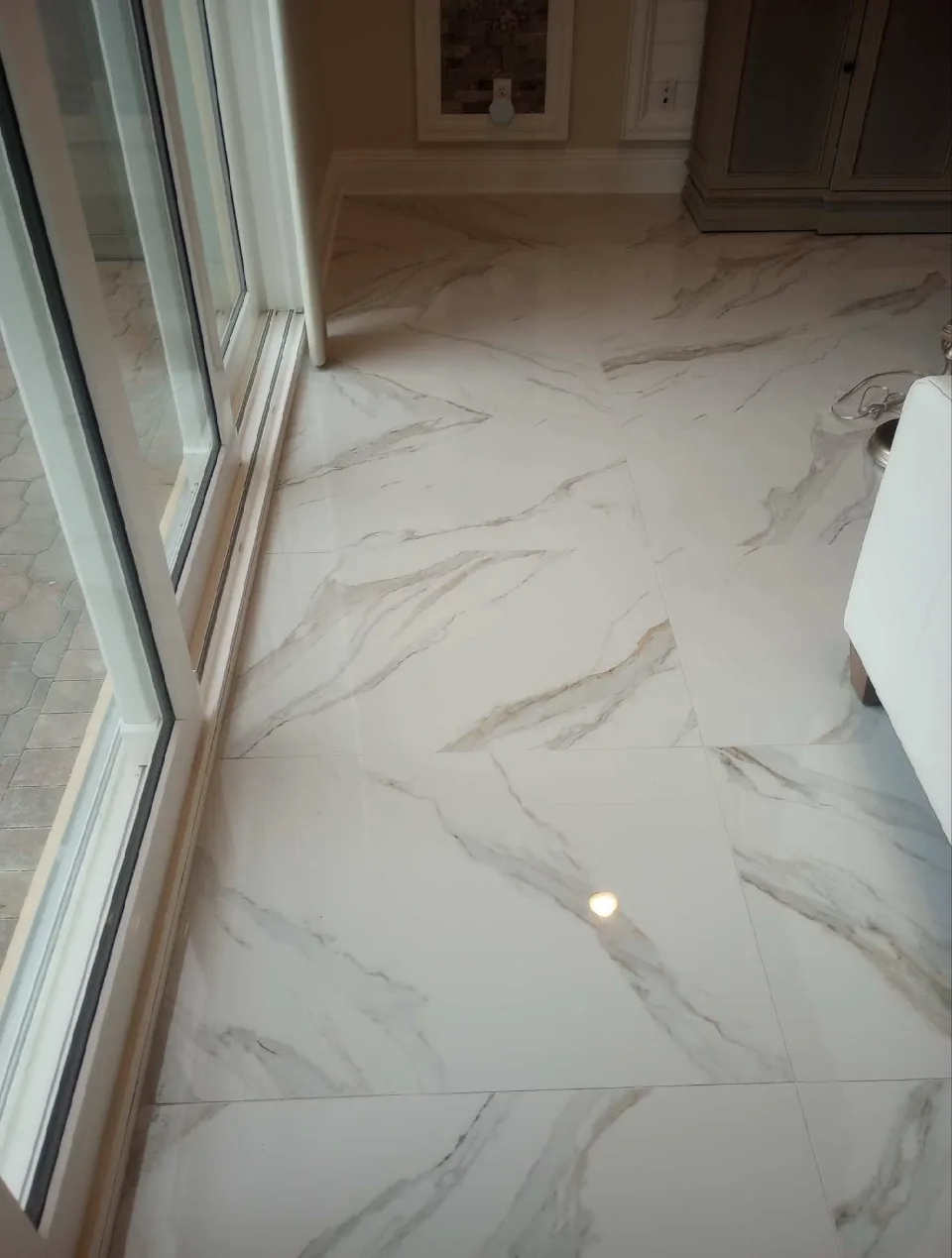 Marble-look polished porcelain floor catching the light beside sliding glass doors